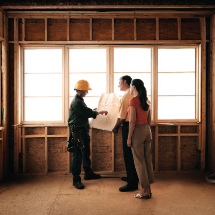 Image of three people, one wearing a construction outfit and pointing to a blueprint