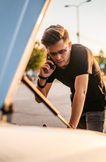 Image of a man with a phone to his ear leaning over a car with the hood open