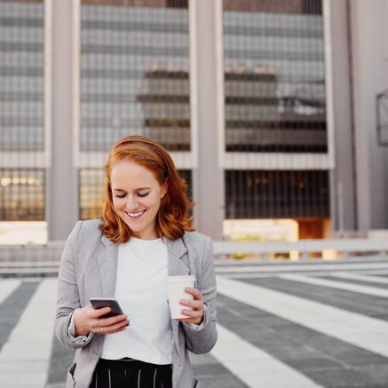 A business woman walking while holding coffee and mobile device.