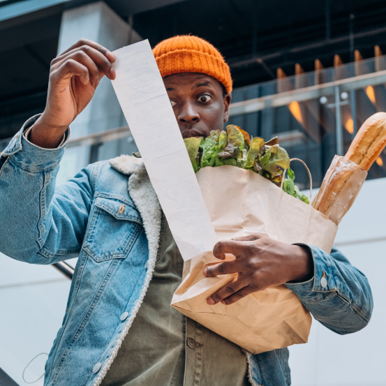 An image of a surprised man holding a bag of groceries looking at a receipt