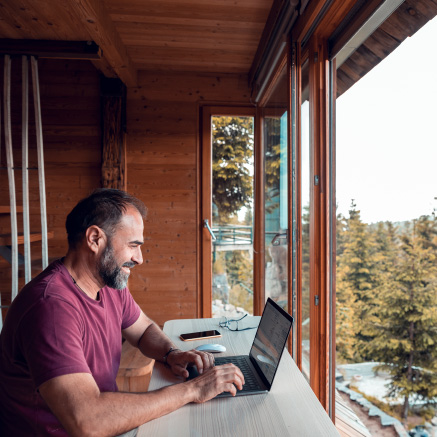A man using a laptop near a large window facing wilderness