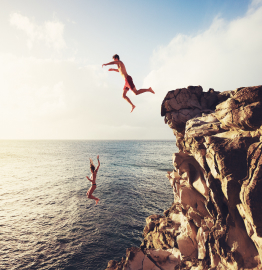 Image of two people jumping off of a cliff into a body of water