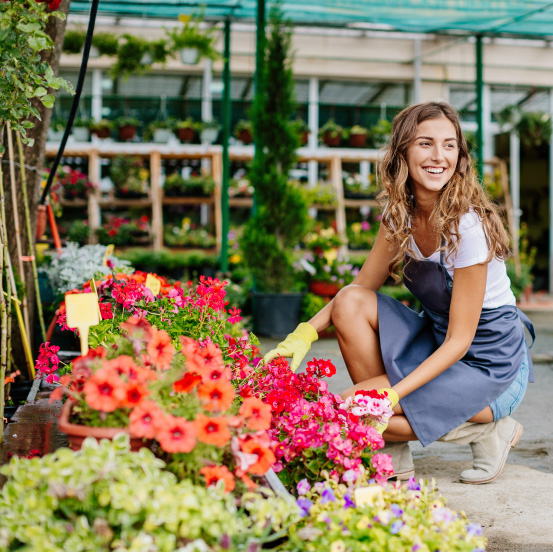 Image of a woman kneeling next to flowers in a greenhouse
