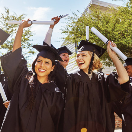 Group of young adults wearing graduation caps and gowns, holding diplomas up in air.