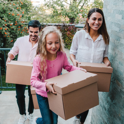 Image of two adults and one child carrying boxes into a house